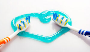 Two toothbrushes positioned on a turquoise heart-shaped dental guide for proper brushing technique.