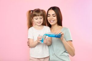 Woman and child using mouthwash together, promoting oral hygiene and dental health.