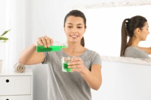 Woman pouring green mouthwash into a glass in a bright bathroom.