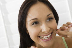 Woman flossing her teeth and smiling, demonstrating proper daily dental hygiene.