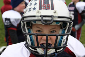 Young football player wearing a white helmet with face mask and protective gear.