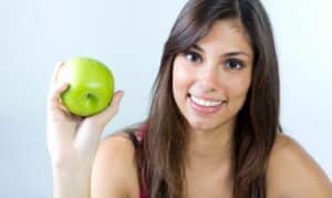Smiling woman holding a green apple for natural teeth whitening benefits.
