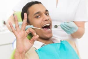 Patient showing stop gesture during dental examination with dentist holding mirror.