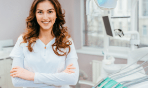 Female dentist with crossed arms smiling in modern dental office treatment room.