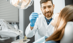 Smiling dentist in blue gloves examining patient during dental sealant consultation.
