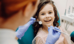 Young girl smiling during a pediatric dental exam with dentist using dental instruments.