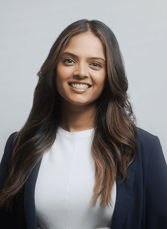 Professional headshot of smiling woman in white shirt and dark blazer against gray background.