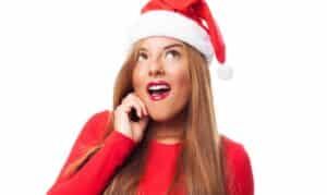 Woman in Santa hat wearing red sweater with bright smile, promoting holiday teeth whitening services.