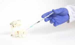 Dentist in blue gloves preparing sedation injection for patient treatment.