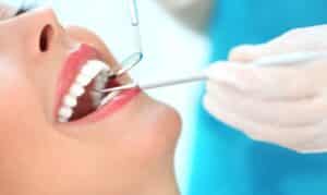 Dentist examining patient's teeth during dental checkup with mirror and tools.