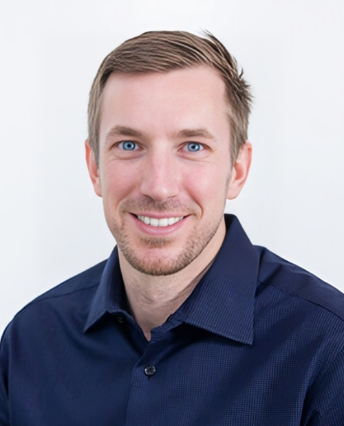 Professional headshot of smiling man in navy button-up shirt against white background.