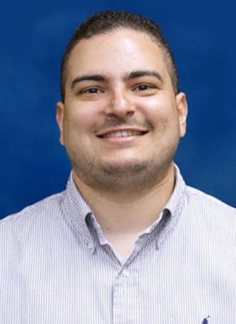 Professional headshot of smiling man in light blue shirt against blue background.