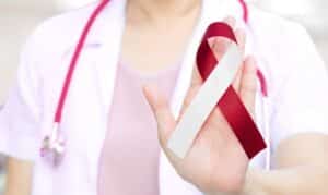 Healthcare provider holding a burgundy and white awareness ribbon for oral cancer prevention.