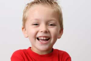 Happy young boy in red shirt smiling, showing healthy primary teeth.