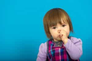 Toddler with hand near mouth demonstrating thumb sucking habit affecting dental development.
