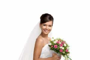 Smiling bride in wedding dress holding bouquet of pink and white roses.