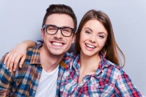 Young couple in plaid shirts smiling brightly, displaying the results of professional teeth whitening.