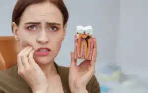 Woman with concerned expression holding a dental model showing tooth decay and nerve damage.