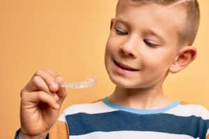 Young boy holding an Invisalign clear aligner, smiling while examining his orthodontic treatment option.