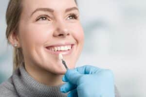 Woman smiling while dentist holds shade guide to match veneer color during consultation.