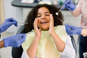 Happy child at dental visit surrounded by dentists in protective gloves during examination.