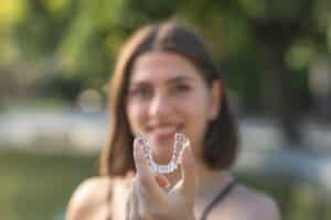 Woman holding clear dental aligner toward camera, demonstrating orthodontic treatment for teeth alignment.
