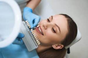 Dentist holding tooth shade guide to patient's smile during cosmetic dental consultation.