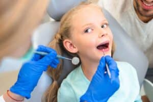 Young girl receiving dental examination with mirror and explorer during pediatric dental visit.